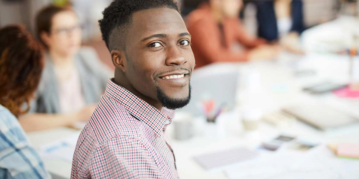 black male in blurry office setting looking back and smiling